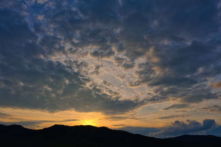 Silhouette of mountains against the background of the shining sun with beautiful cloudsの写真素材