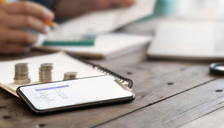 Planning monthly home budget concept. Smartphone with a list of expenses for the month on wooden tableの写真素材