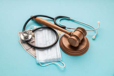 Wooden judge gavel with medical mask, doctor's stethoscope and money on blue background. Healthcare legislation and medical conceptの写真素材