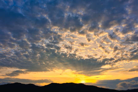 Silhouette of mountains with beautiful sunset with the bright setting sun breaking through the cloudsの写真素材