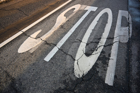 Top view of a white stop traffic sign painted on weathered and cracked black asphalt pavement. High...