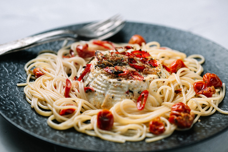 Spaghetti with roasted ricotta and tomatoes on a black plateの写真素材