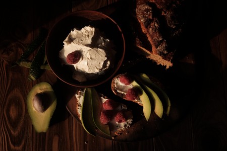 Bread and toasts with cream cheese, raspberries and avocado on wood backgroundの写真素材
