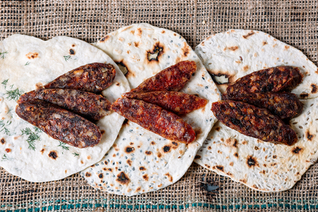Three pitas with pieces of salami on a wooden cutting board on a brown canvasの写真素材