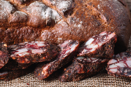 Pieces of smoked salami with rye bread on a brown canvasの写真素材
