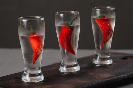 Cold vodka in a shot glass on a wooden cutting board on dark backgroundの写真素材