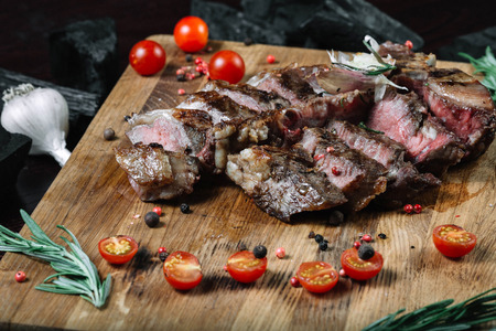 Sliced ??grilled T-bone steak tomatoes on a cutting board on dark backgroundの写真素材