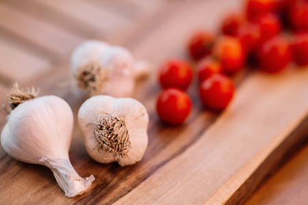 Three garlic cloves and cherry tomatoes on wood backgroundの写真素材