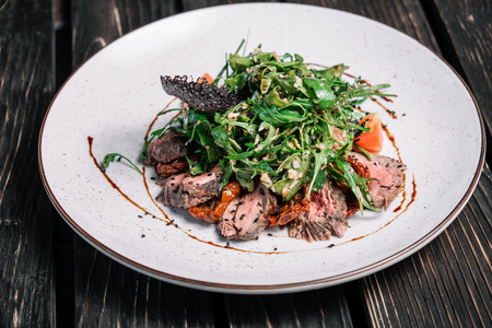 Salad with warm veal, sun-dried tomatoes and arugula on dark wooden backgroundの写真素材