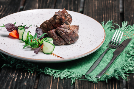 Grilled beef steak served with green napkin and cutlery on dark wooden backgroundの写真素材