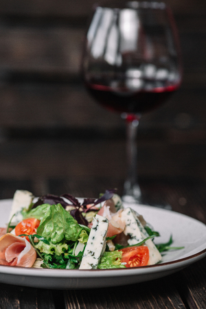Glass of wine and green salad with prosciutto and blue cheese on dark wooden backgroundの写真素材