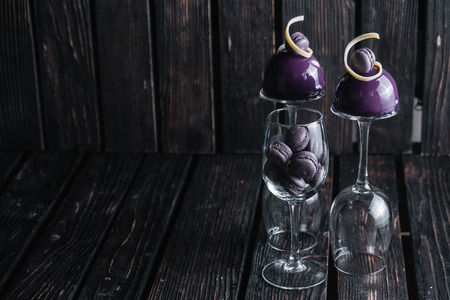 French blueberry mousse cake served on inverted wine glasses and macaroons in one of these on wood background. Dessert decorated of chocolate spiral and macaroonsの写真素材