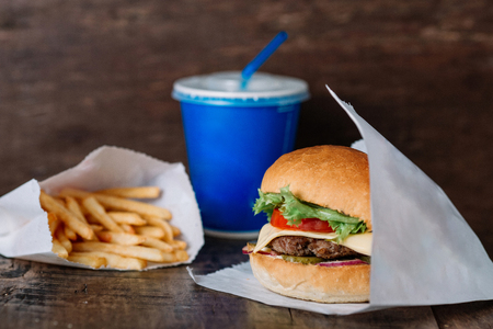 fresh tasty burger wrapped on white paper and french fries on wooden table. With empty place for titleの写真素材