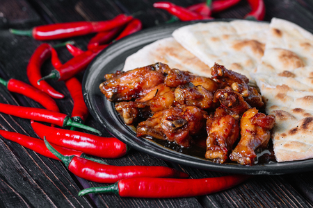 Juicy fried chicken wings with flatbread and chilli peppers on dark wood backigroundの写真素材
