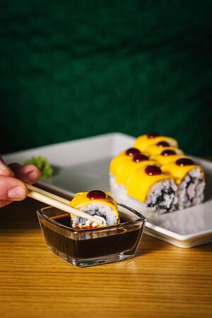 Men's hands hold sushi with chopsticks over plateの写真素材