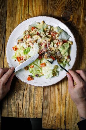Male hands hold a knife and fork over vegetable saladの写真素材