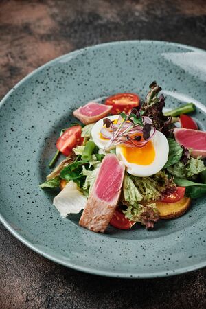 warm salad with beef, tomatoes and egg on top on a dark backgroundの写真素材