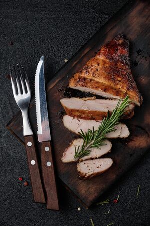 Grilled chicken fillets on wooden cutting board with rosemary and cutlery on black background. Top viewの写真素材