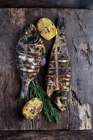 Grilled trout and dorado served on a cutting board. On wooden background. Top viewの写真素材