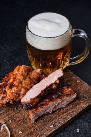 Cutted pork ribs and big glass of beer on cutting board on dark on concrete backgroundの写真素材