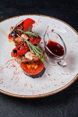 Grilled veal and grilled vegetables on a white plate and cherry sauce on a dark concrete backgroundの写真素材