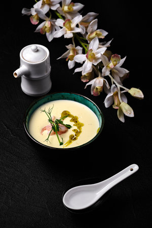 Bowl of Cheese soup with shrimps and flower of orchid on black backgroundの写真素材