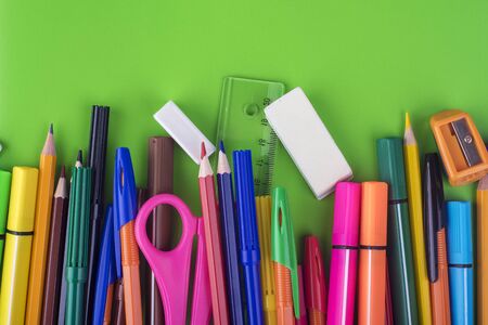 On a green background colored pencils and pens, office stationery
