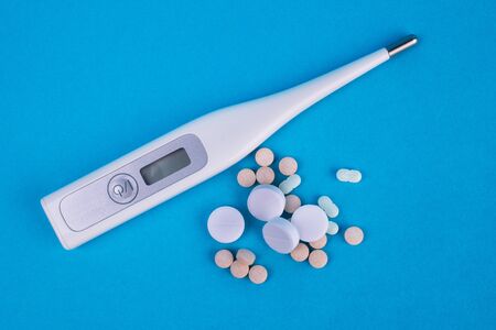 Thermometer and white tablets on a blue background