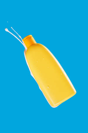 Yellow bottle of cream on a blue background with cream splashes in different directions, levitation