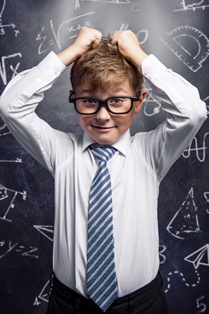 School. Boy with glasses on the background of a blackboard holding his head