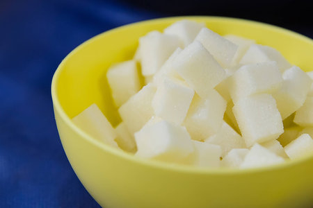 Sugar refined cubes in a yellow plate on a blue tableの写真素材