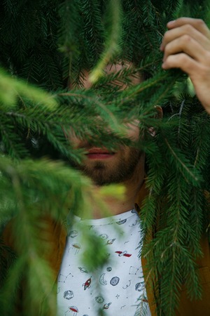 Young cute stylish guy dreams in green and lush fir branches on a summer dayの写真素材