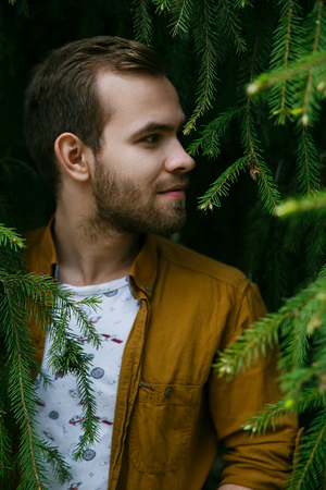 Young cute stylish guy dreams in green and lush fir branches on a summer dayの写真素材