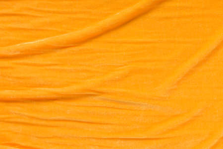 Colored orange textile satin fabric folded in folds and waves with highlights and texture shimmers in the lightの写真素材