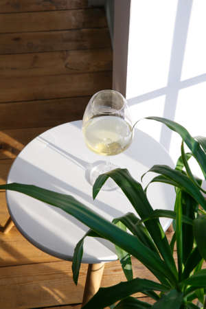 One glass of white wine is on the side table near the windowの写真素材