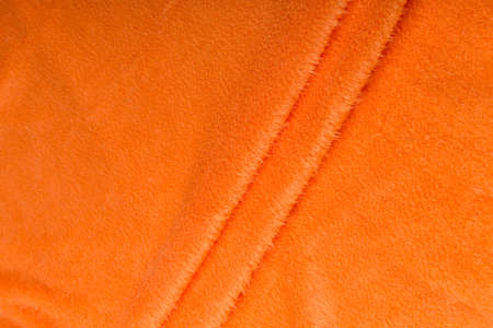 Colored orange textile satin fabric folded in folds and waves with highlights and texture shimmers in the lightの写真素材