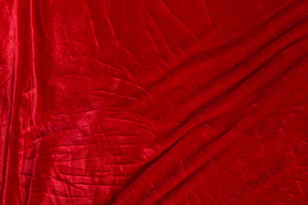 Colored red textile satin fabric folded in folds and waves with highlights and texture shimmers in...