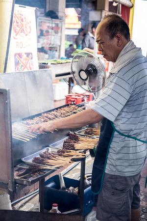 Satay seller tending his satay stall and making sure the satay is properly grilled. Satay is seasoned meat or chicken skewered with bamboo stickのeditorial素材