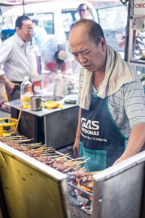 Satay seller tending his satay stall and making sure the satay is properly grilled. Satay is seasoned meat or chicken skewered with bamboo stickのeditorial素材