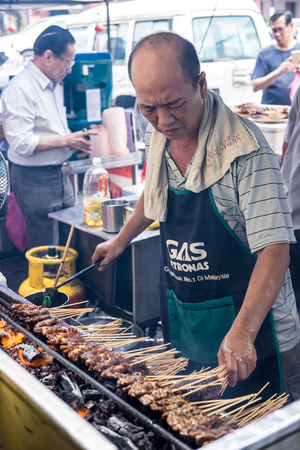 Satay seller tending his satay stall and making sure the satay is properly grilled. Satay is seasoned meat or chicken skewered with bamboo stickのeditorial素材