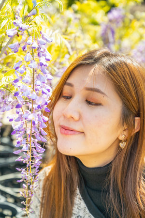 Tokyo, Japan - April 15, 2024: Girl poses with wisteria flowers in the garden.の写真素材