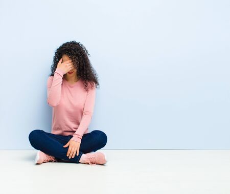 young pretty woman looking stressed, ashamed or upset, with a headache, covering face with hand sitting on floorの写真素材