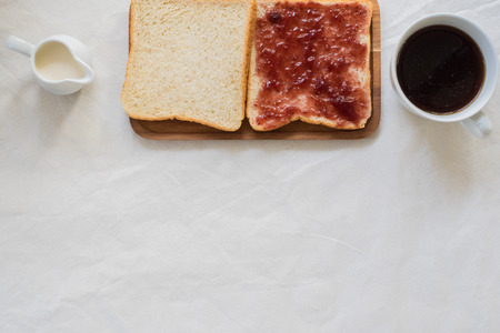 A set of Breakfast including cup of coffee with milk cream and sliced bread with raspberry jam on white tablecloths with space for textの写真素材