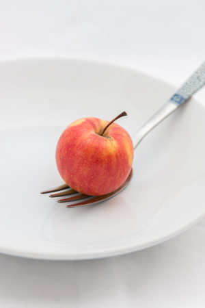 Small apple with fork on a white plate with large leaves.の写真素材