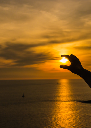 Hands and fingers hold  sun at sunset over ocean.の写真素材