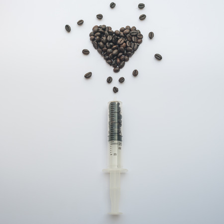 Heart shaped coffee beans and syringe concept on white background.の写真素材