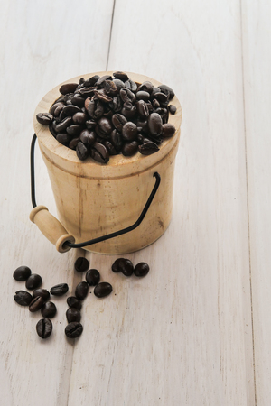 Coffee beans in a small wooden bucket on white wood table.の写真素材