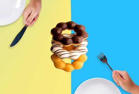Donut eating concept using a knife and fork on pastel.