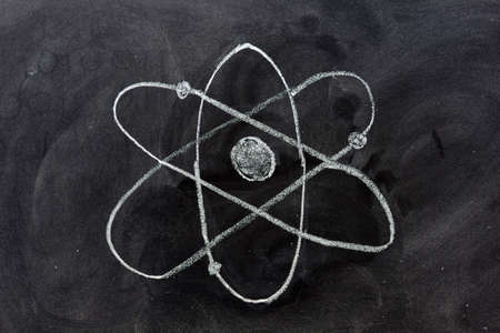 Hand pointing at the atom symbol drawn in chalk on a blackboardの写真素材