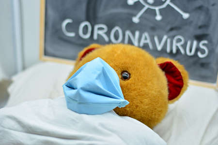 Coronavirus sick teddy bear, isolated, in a hospital bed, wearing a maskの写真素材